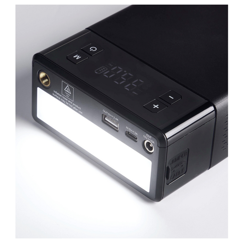 Ein schwarzes elektronisches Gerät mit Display, Knöpfen und mehreren Anschlüssen, darunter USB und DC Out, auf einer weißen Oberfläche.